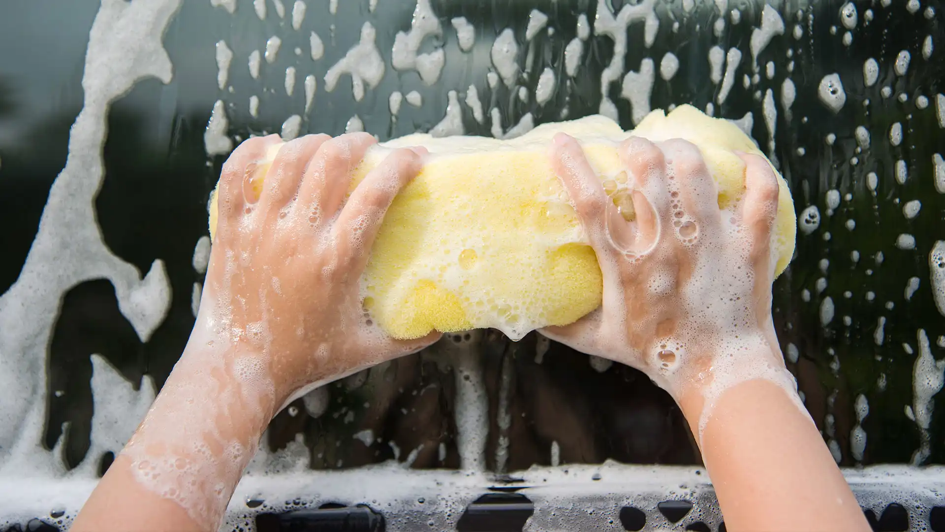 Up close hands holding a sponge and cleaning soap off of a car window