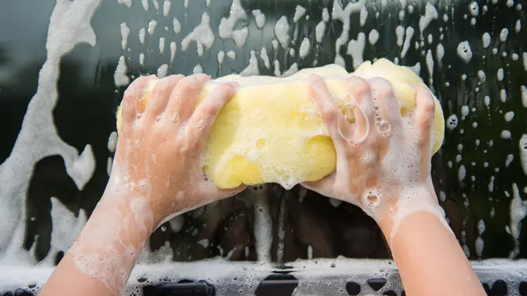 Up close hands holding a sponge and cleaning soap off of a car window