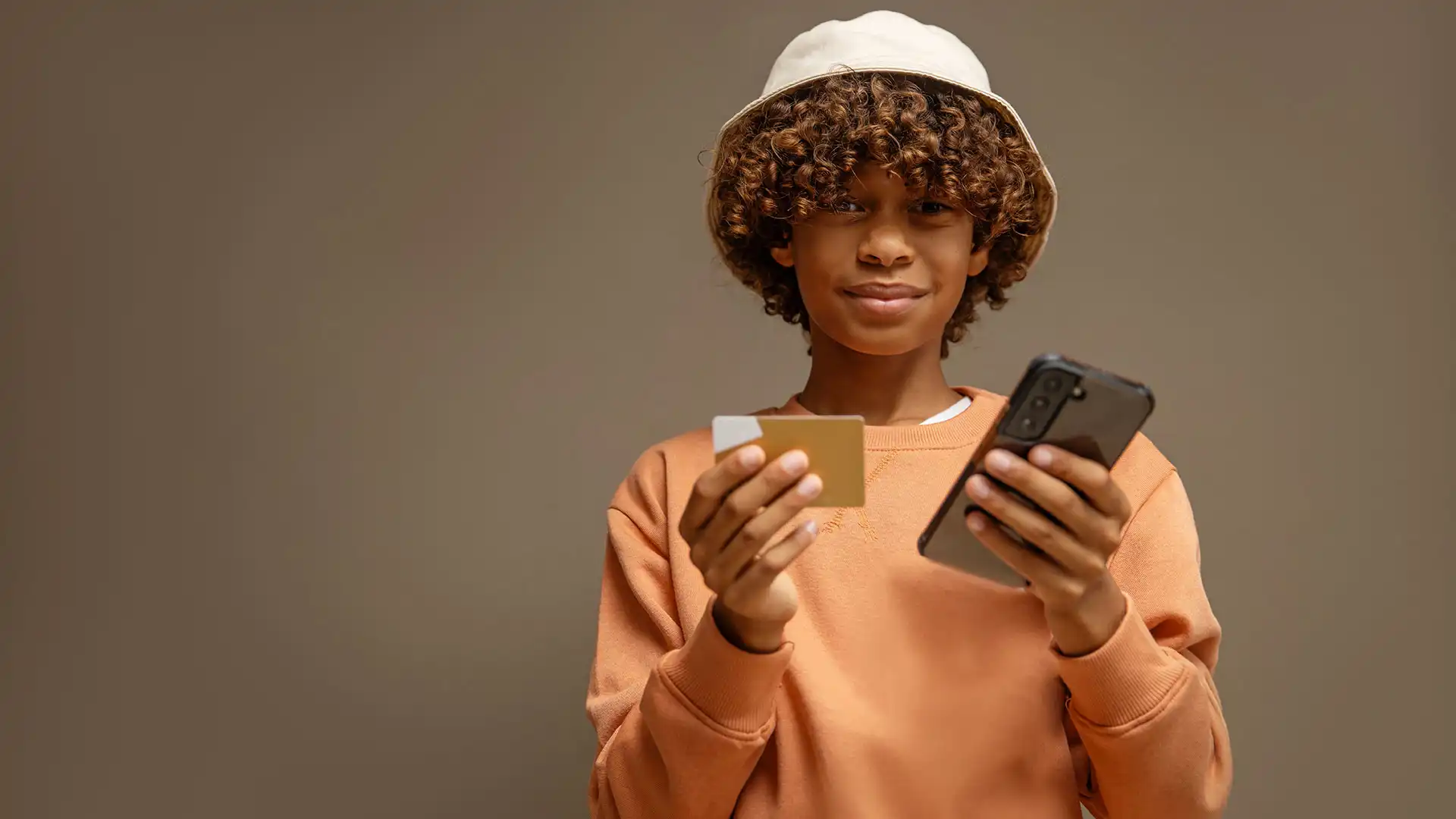 Boy stands with a credit card in one hand and his mobile in the other